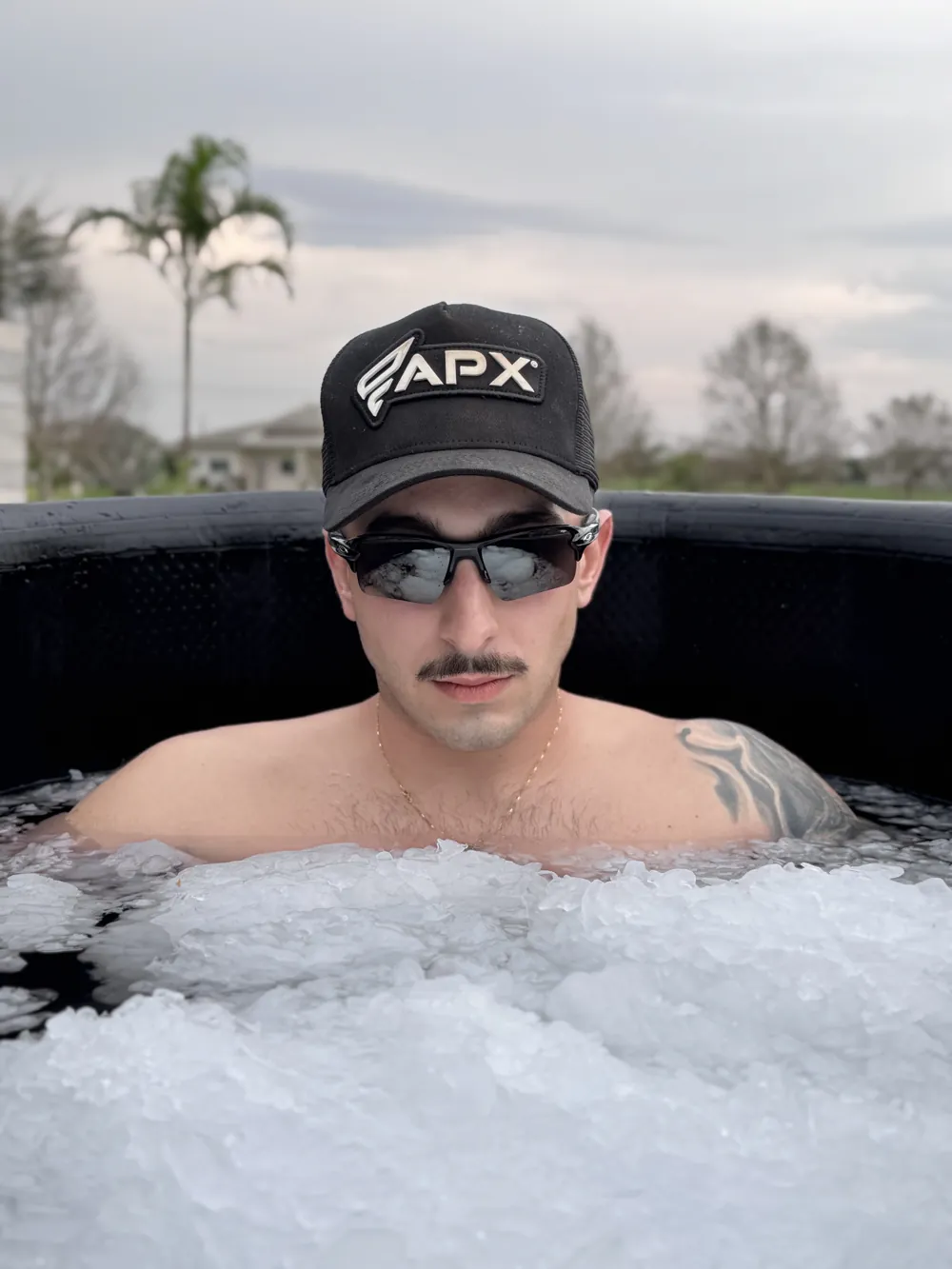 João Bêrnardino dentro de uma banheira de gelo da Apex, com boné e óculos escuros, com gelo até o peito
